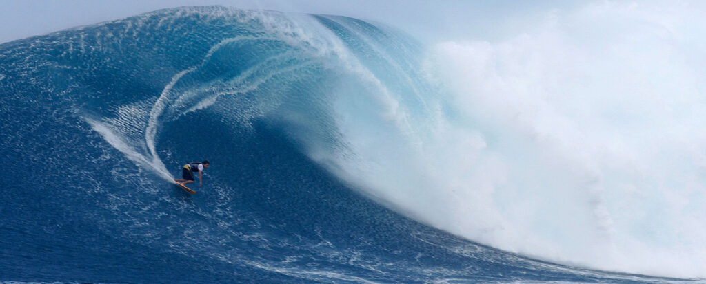 A surfer rides along the face of a large breaking wave.