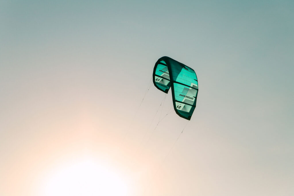 A teal kiteboarding kite floats against a pastel sky.
