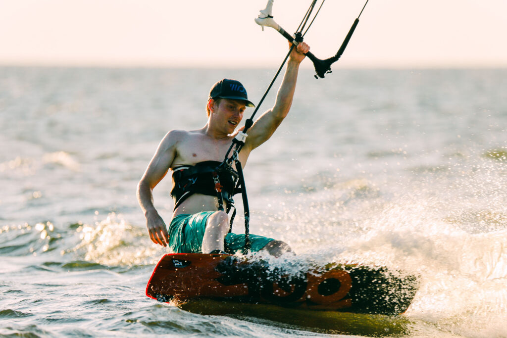 A man kiteboards across choppy water with spray around his board.