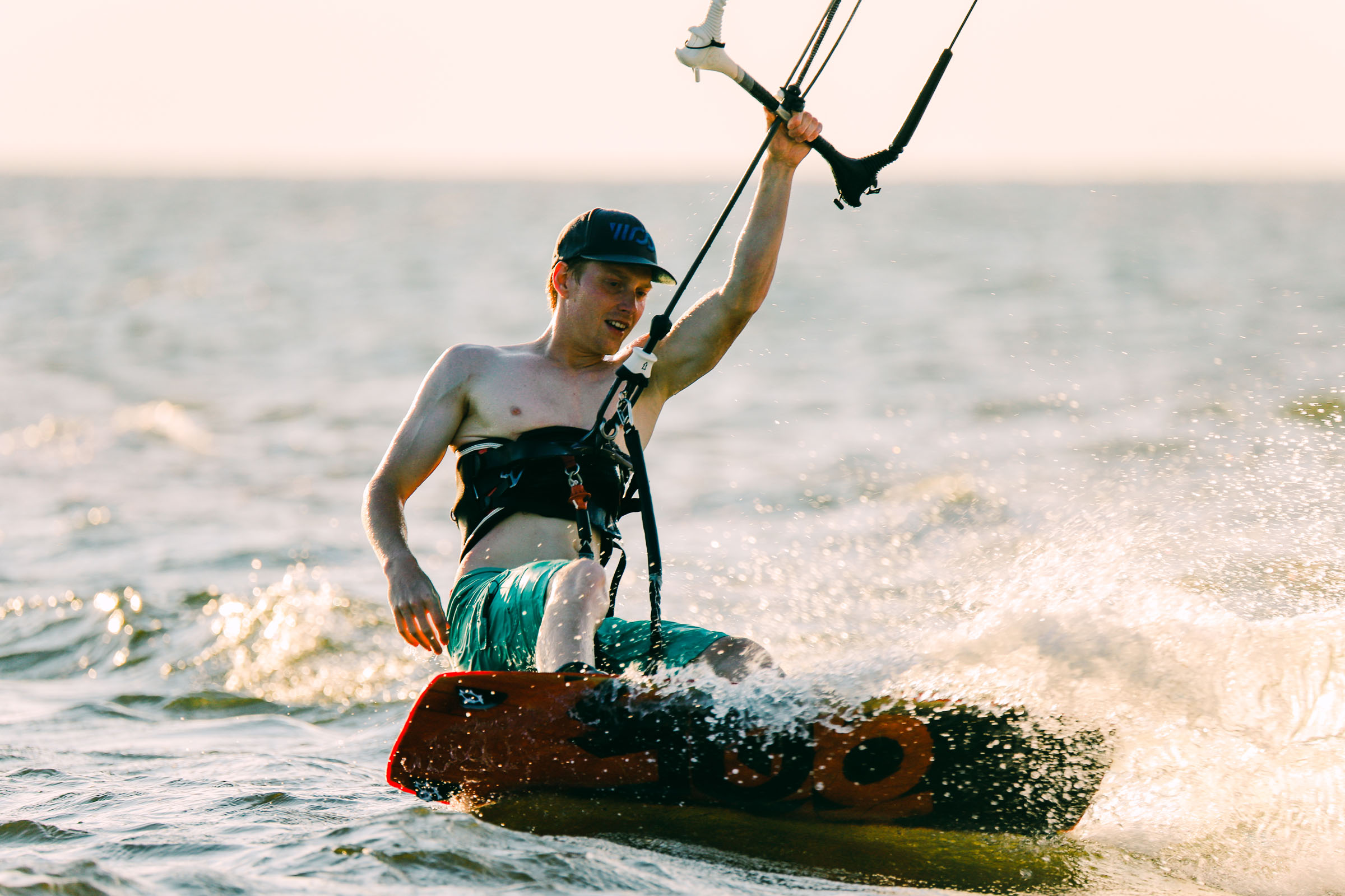 A man kiteboards across choppy water with spray around his board.