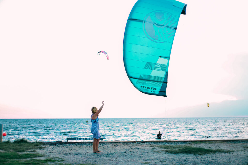 A person stands on the beach guiding a large kite over the water.