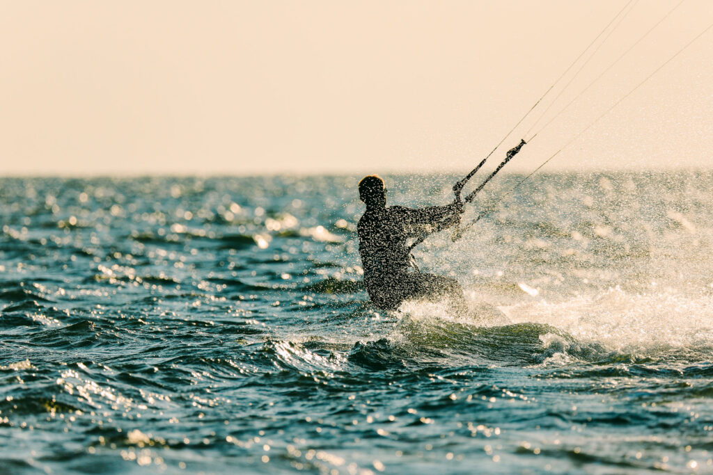 A kiteboarder rides across choppy water with spray kicking up around them.