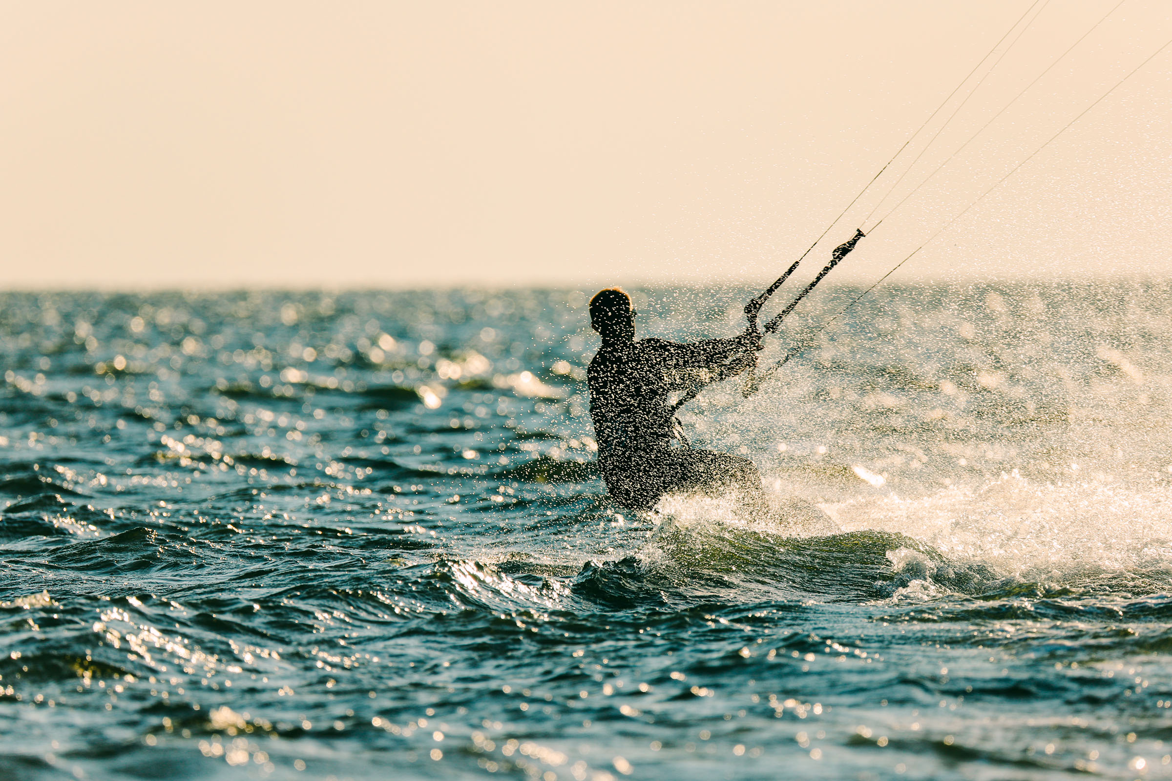 A kiteboarder rides across choppy water with spray kicking up around them.