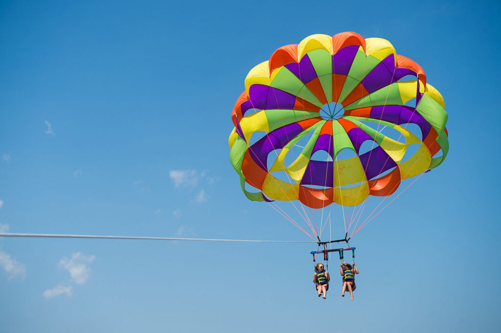 Two people hang beneath a colorful parasail against a clear blue sky.