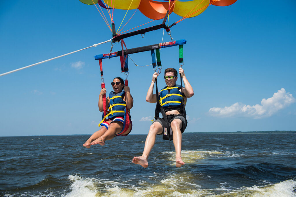 Two people parasail above the water on a sunny day.