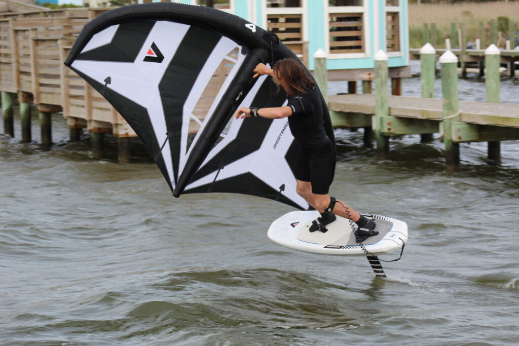 A person wing foils on choppy water beside a dock in the Outer Banks.